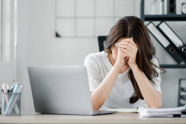 Eine Frau sitzt an einem Schreibtisch mit Laptop und Notizbuch. Sie blickt mit traurigem Gesichtsausdruck auf den Laptop-Bildschirm - Foto, Bild