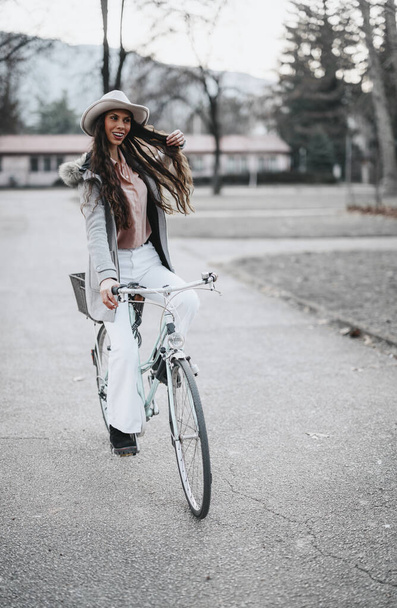 Egy stílusos, profi nő biciklivel pihentető utazást tesz egy nyugodt parkban, megtestesítve a munka és a magánélet egyensúlyát.. - Fotó, kép