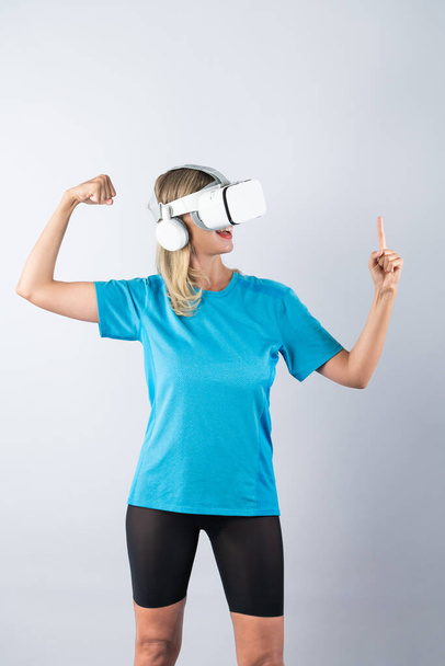 Девушка указывает или крутит баскетбол, используя очки VR. Белая женщина сгибается в повседневной рубашке, очках визуальной реальности и стоит на розовом фоне. Инновации. Контрапция. - Фото, изображение