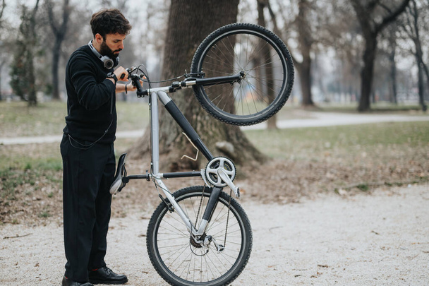 Ένας εστιασμένος επιχειρηματίας με επίσημη ενδυμασία επισκευάζει το ποδήλατό του σε εξωτερικούς χώρους, επιδεικνύοντας ισορροπία μεταξύ εργασίας και ζωής. - Φωτογραφία, εικόνα