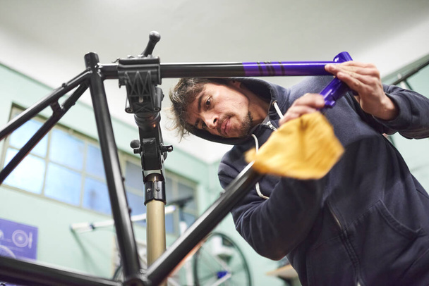Hispanic young man working on a custom bike frame painting design in purple and black, a creative and technical handcrafted process, in his workshop. - Photo, Image