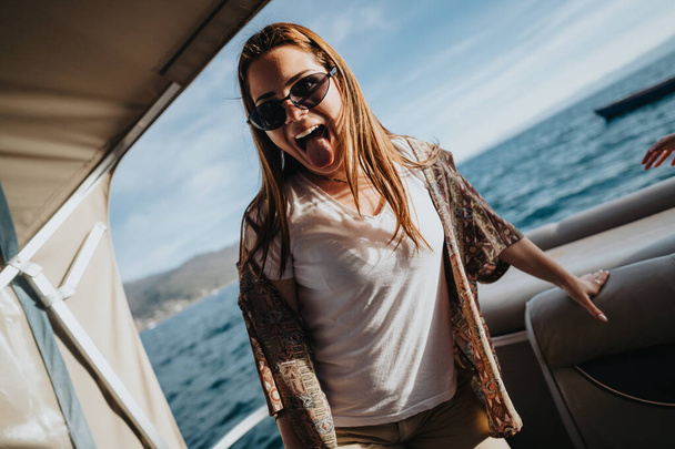 Ein glückliches Mädchen drückt seine Freude aus, als sie auf einem Boot steht und sich in der Wärme eines sonnenbeschienenen Tages auf dem Meer sonnt. - Foto, Bild