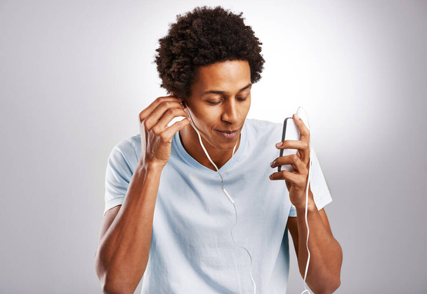 Musta mies kuuntelee musiikkia ja kännykkää, jossa on ääni, radio ja suoratoisto valkoisella studiotaustalla. Afrikkalainen henkilö, kaveri ja malli älypuhelimella ja yhteys digitaaliseen sovellukseen ja ääneen. - Valokuva, kuva
