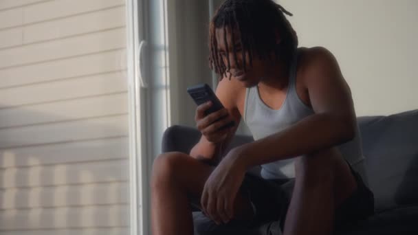 A man with dreadlocks typing on his phone at home at sunset. Slow motion.  - Footage, Video