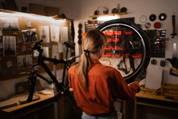 Mujer joven que trabaja en un taller de reparación de bicicletas, reparación de bicicletas. Copiar espacio - Foto, Imagen