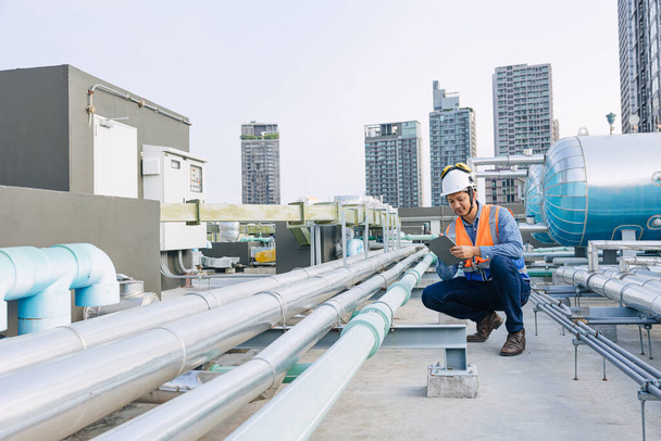 engineer male technician worker working service hotel boiler tank hot water supply pipe system. man safety checking maintenance pipeline heating water delivery line at roof top outdoor. - Photo, Image