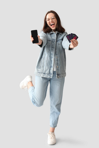 Beyaz arka planda kredi kartları ve cep telefonu olan genç bir kadın. İnternetten alışveriş - Fotoğraf, Görsel
