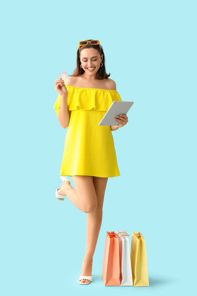 Giovane donna con carta di credito, tablet moderno e shopping bag su sfondo blu - Foto, immagini