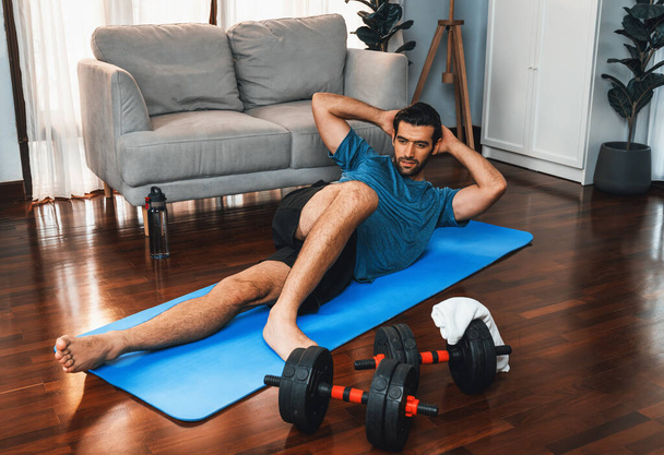Atlétikai és sportos férfi csinál ropogós fitness mat alatt otthoni testedzés edzés edzést a fitt fizikum és az egészséges sport életmód otthon. Vidám otthoni edzés képzési koncepció. - Fotó, kép
