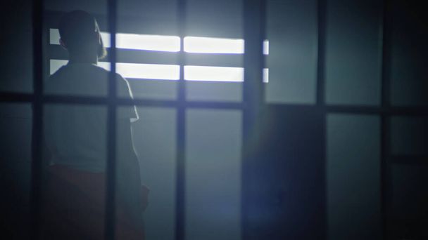 Narancssárga egyenruhás férfi járkál a cellában, aztán leül az ágyra és elkezdi olvasni a Bibliát. Vallásos rab börtönben tölti a büntetését. Fogolytábor vagy büntetés-végrehajtási intézet. - Fotó, kép