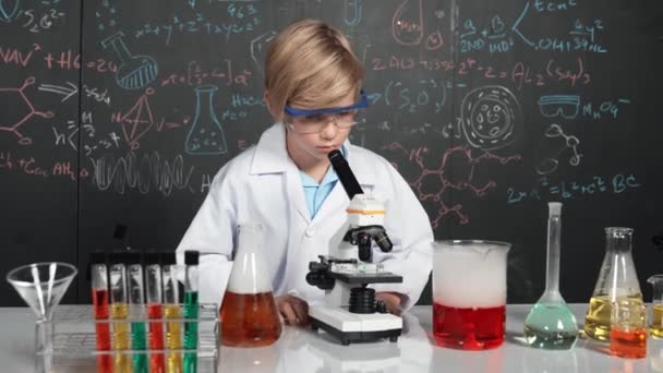Mądry chłopiec korzystający z próbki analizy mikroskopowej w laboratorium naukowym na zajęciach z chemii. Szczęśliwy student rasy kaukaskiej patrzący pod lupę, by zbadać płyn chemiczny w probówkach. Erudycja. - Materiał filmowy, wideo