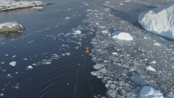 Badacze polarni w łodzi motorowej pływają między górami lodowymi na Antarktydzie. Niebezpieczne - ludzie boją się utknąć. Lot drona nad krajobrazem oceanu. Gumowe łodzie motorowe pływające w zuchwałym lodzie. - Zdjęcie, obraz