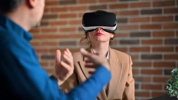 Mujer usando un auricular de realidad virtual en una oficina mientras explica y gesticula - Imágenes, Vídeo