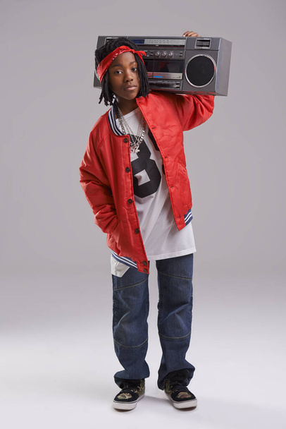Африканский мальчик, хип-хоп и модный портрет с радио для рэп-музыки и танцев в студии с городской одеждой. Черный ребенок и бумбокс с модной одеждой и шиком с уверенностью и серым фоном. - Фото, изображение