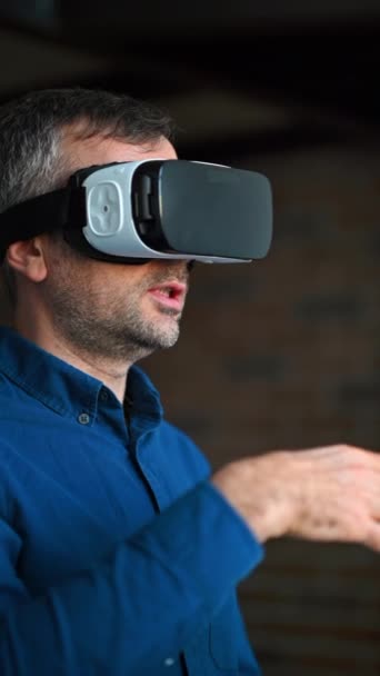Mann gestikuliert, während er ein Virtual-Reality-Headset im Büro benutzt. Vertikal - Filmmaterial, Video