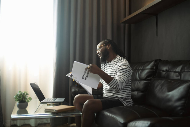 Занятой афроамериканец читает отчет или контракт и разговаривает по мобильному телефону дома. - Фото, изображение