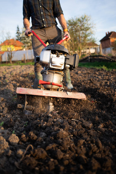 agriculture biologique homme laboure le sol au coucher du soleil avec un tiller préparant le sol pour l'ensemencement - Photo, image