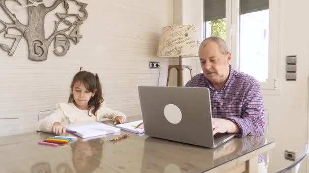 Video de una chica para colorear con su abuelo mientras trabaja en un ordenador portátil en casa - Metraje, vídeo