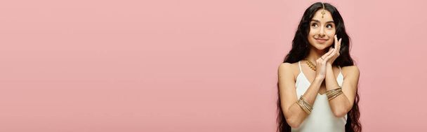 Kiehtova intialainen nainen, jolla on pitkät hiukset, aiheuttaa kauniisti elinvoimaista vaaleanpunaista taustaa vasten.. - Valokuva, kuva