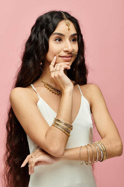 Captivating indian woman with long hair poses with gold jewelry on pink backdrop. - Photo, Image