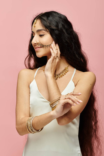 Mulher indiana elegante com cabelos longos e jóias de ouro marcando uma pose contra um pano de fundo rosa. - Foto, Imagem