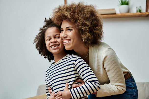 Una madre y una hija afroamericanas felices abrazan cariñosamente en un sofá acogedor en casa. - Foto, Imagen