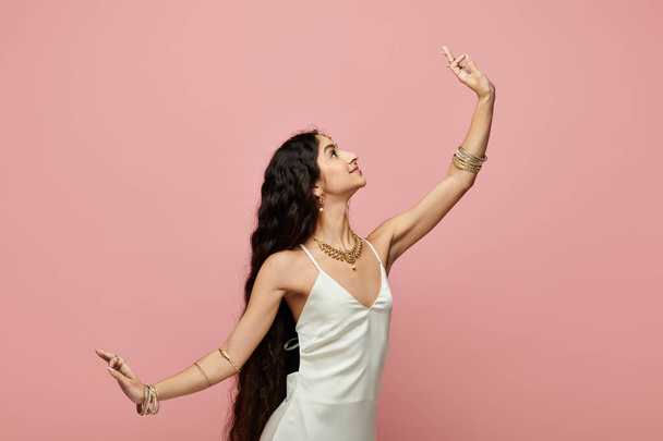 A young indian woman poses gracefully in a white dress against a striking pink backdrop. - Photo, Image
