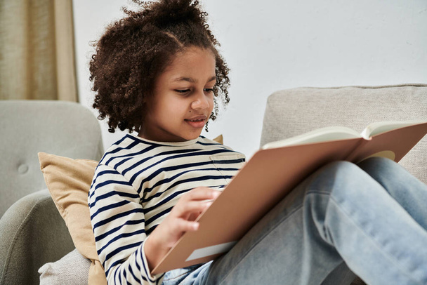 Ein junges Mädchen, in ein Buch vertieft, sitzt auf einer gemütlichen Couch - Foto, Bild