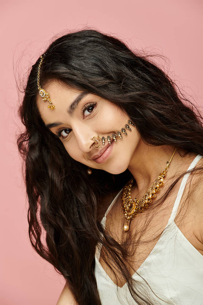 Jeune femme indienne aux cheveux longs et bijoux en or pose élégamment pour la caméra. - Photo, image