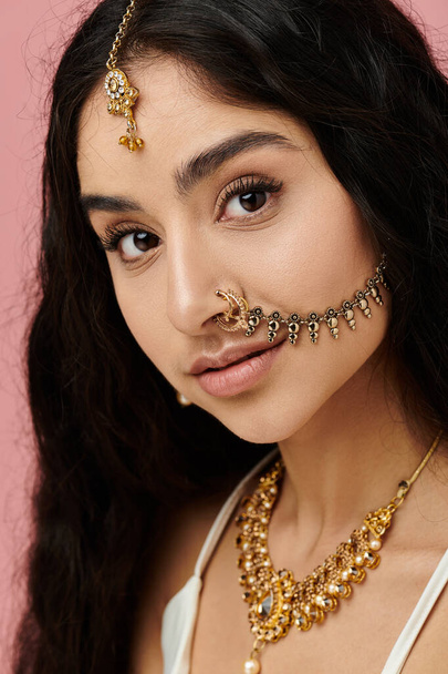 Молодая индианка демонстрирует свою красоту с золотыми украшениями и кольцом в носу. - Фото, изображение