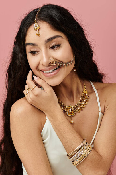 Jeune femme indienne aux cheveux longs et bijoux en or pose gracieusement sur un fond rose vif. - Photo, image