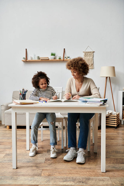 Een gelukkige Afro-Amerikaanse moeder en dochter zitten aan een tafel, genietend van quality time samen in hun woonkamer. - Foto, afbeelding