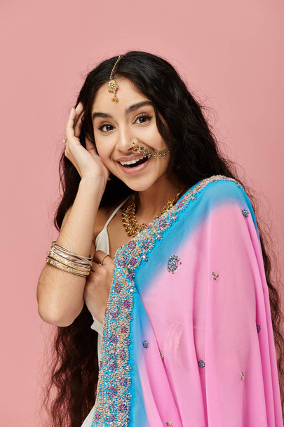Молодая индианка в розовом и синем сари изящно позирует для портрета. - Фото, изображение