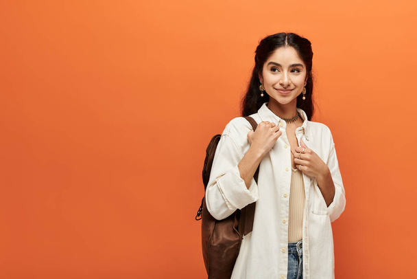 Young indian woman with backpack striking a pose against bright orange background. - Photo, Image