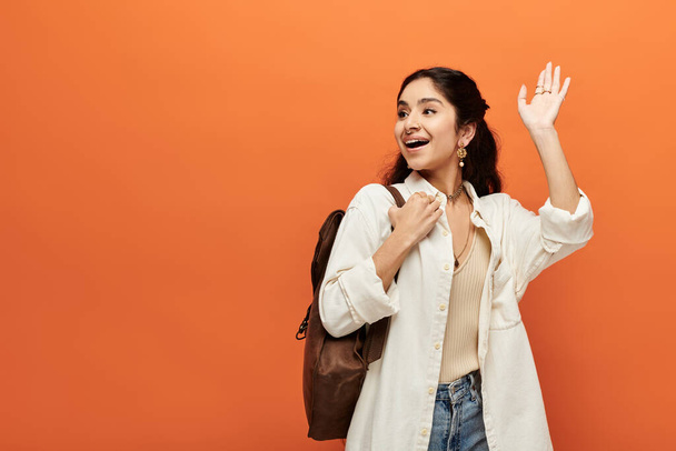 A young indian woman energetically waves hand against orange background. - Photo, Image