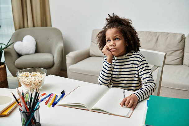 Молода дівчина афроамериканського походження сидить за столом з книгою і ручками, занурена в її мрії - Фото, зображення