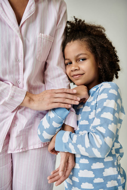 Happy African American mother and daughter in pajamas enjoying quality time together on a grey background. - Photo, Image
