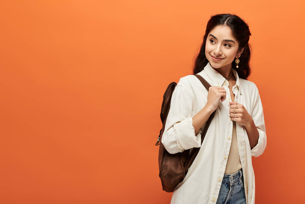 Jeune femme indienne se tient avec confiance avec un sac à dos sur fond orange vif. - Photo, image