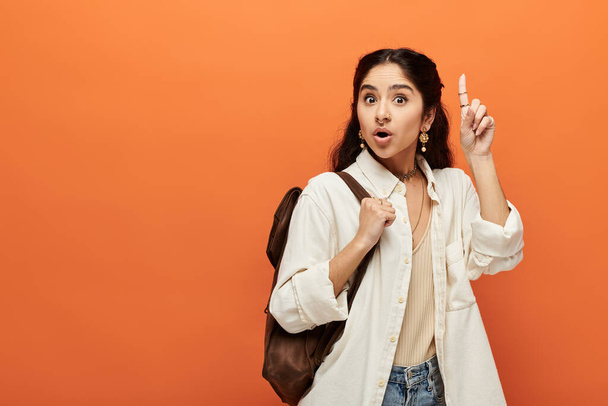 Young indian woman energetically pointing finger in front of bright orange background. - Photo, Image