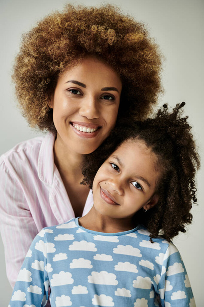 Una felice madre e figlia afroamericana posano insieme in pigiama abbinato su uno sfondo grigio. - Foto, immagini