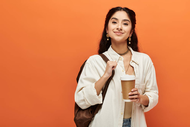 Молодая индианка наслаждается чашкой кофе на оранжевом фоне. - Фото, изображение