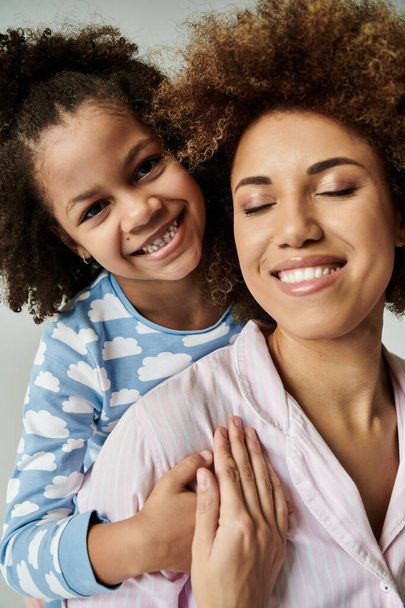 Afroamerykańska matka i córka w piżamie uśmiechające się szczęśliwie razem na szarym tle. - Zdjęcie, obraz