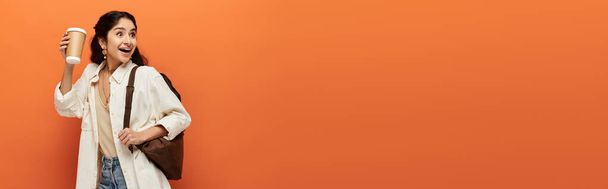 Una donna indiana elegante posa con un cellulare su uno sfondo arancione audace. - Foto, immagini