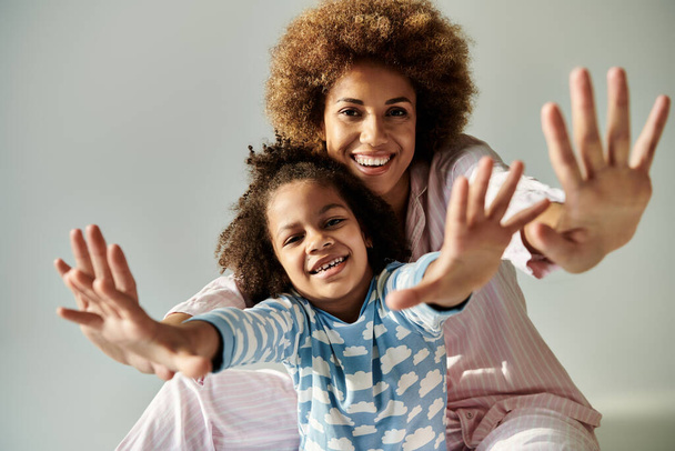A happy African American mother and daughter in pajamas posing together on a grey background. - Photo, Image