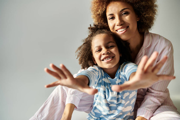 Una feliz madre afroamericana y su hija en pijama posan juntas para la cámara sobre un fondo gris. - Foto, imagen