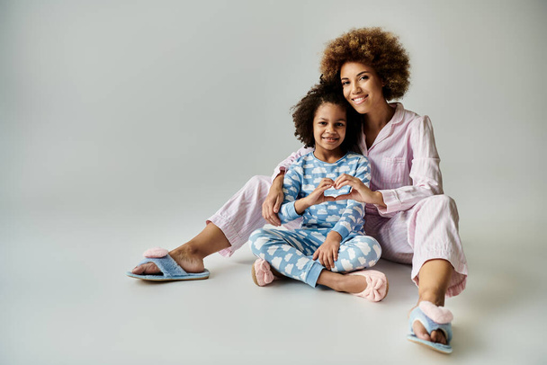 Boldog afro-amerikai anya és lánya ül szorosan a padlón megfelelő pizsamában, megosztva egy különleges pillanatot. - Fotó, kép