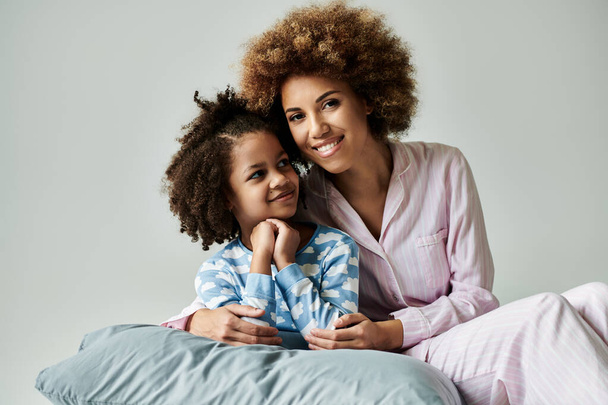 Een Afro-Amerikaanse moeder en dochter in pyjama poseren graag voor een foto op een grijze achtergrond. - Foto, afbeelding