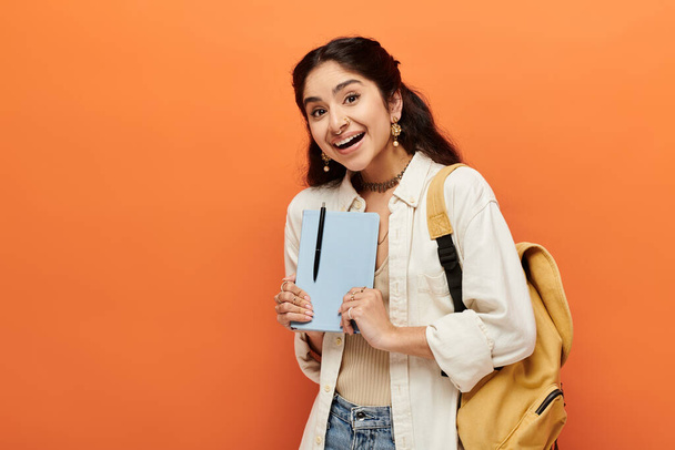 Fiatal indiai nő magabiztosan tartja notebook narancssárga háttér. - Fotó, kép