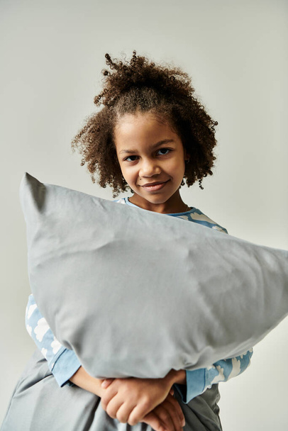 Una giovane ragazza che abbraccia gioiosamente un soffice cuscino su uno sfondo bianco sereno. - Foto, immagini