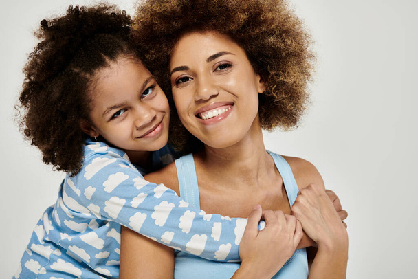 Щаслива афроамериканська мати і дочка в піжамі позує разом на сірому фоні. - Фото, зображення
